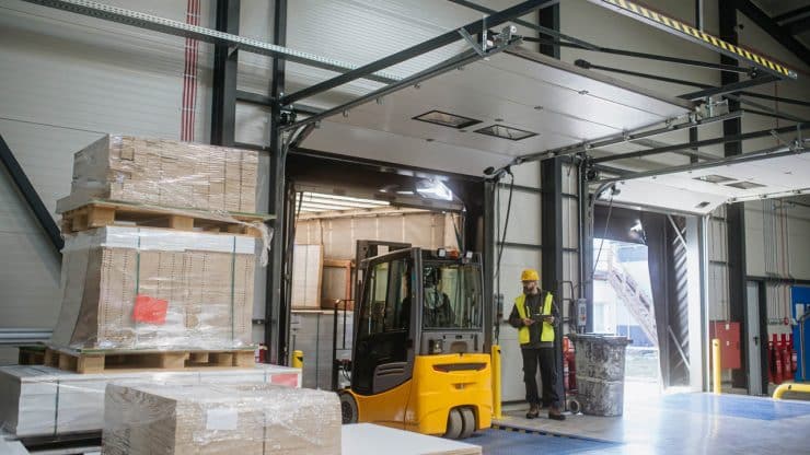 Warehouse receiver overseeing the storing of delivered items holding tablet looking at cargo details Forklift carrying pallets with goods